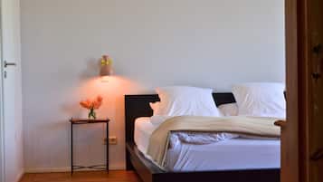 Ein Schlafzimmer mit einem Bett, einem Nachttisch mit Blumenvase und einer Wandleuchte.