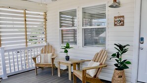 A wooden deck with two chairs and a table, a potted plant, and a 'Positive Waves' sign on the wall.