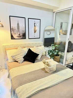 A bedroom with a bed, pillows, a bedside table, a clock, and two framed pictures on the wall. - Azure Create Greate Moments by Don (Paranaque)