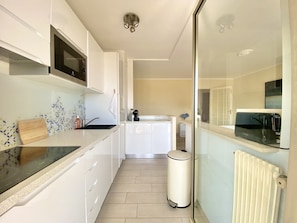 Una cucina moderna con mobili bianchi, un forno a microonde, un lavello e un cestino.