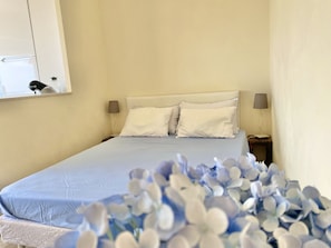 Un letto rifatto con una coperta azzurra e due cuscini, una lampada da comodino e uno specchio sulla parete.