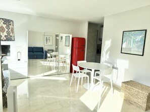 Una cucina moderna con elettrodomestici bianchi, una zona pranzo con sedie bianche e un divano blu nella zona living.