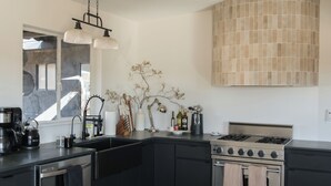 Une cuisine moderne avec des meubles de couleur sombre, une cuisinière à gaz, un lave-vaisselle et un grand miroir au-dessus de l’évier.