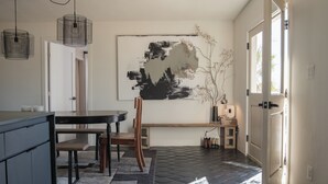 Une cuisine moderne avec un coin repas, agrémentée d’un tableau abstrait en noir et blanc, d’un banc en bois et d’un sol imitant la pierre.
