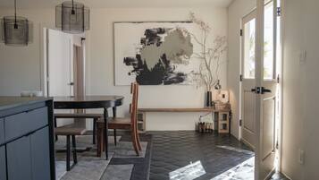 A modern kitchen with a dining area, featuring a black and white abstract painting, a wooden bench, and a stone-patterned floor.
