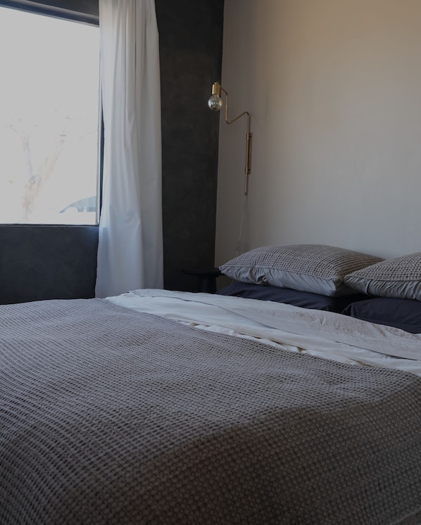 A bedroom with a bed, pillows, a nightstand, a lamp, and a window with curtains.