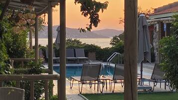 A poolside area with lounge chairs, a pergola, and a view of the sea at sunset.