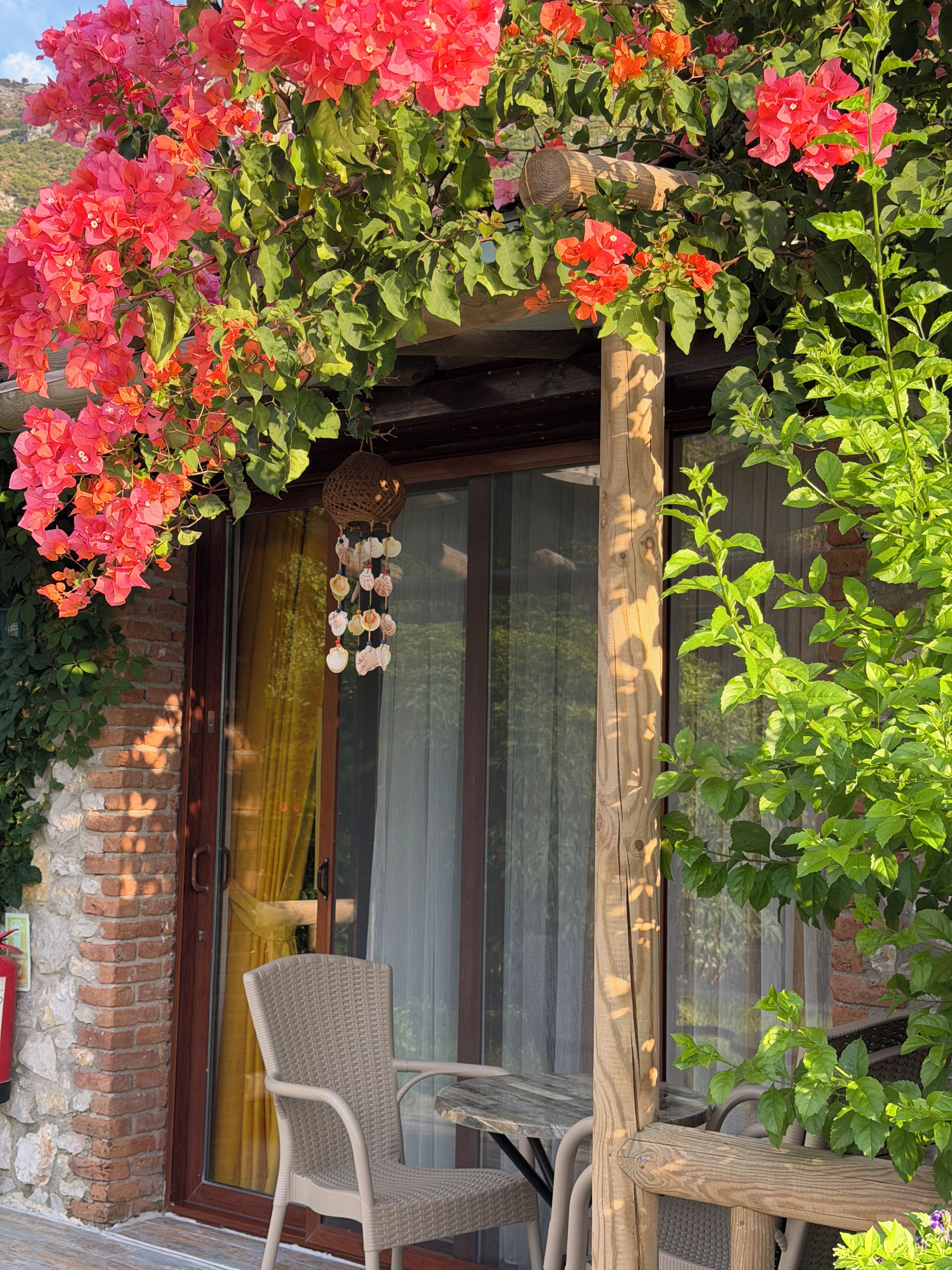 A patio with a wooden table and chairs, a glass door, and a wall covered with flowering plants.