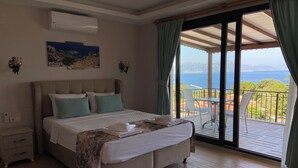 Un dormitorio con cama, mesita de noche, aire acondicionado mural, un cuadro y un balcón con vistas al mar.
