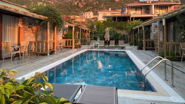 Zona de piscina con sillones de descanso, terraza de madera y montañas al fondo.