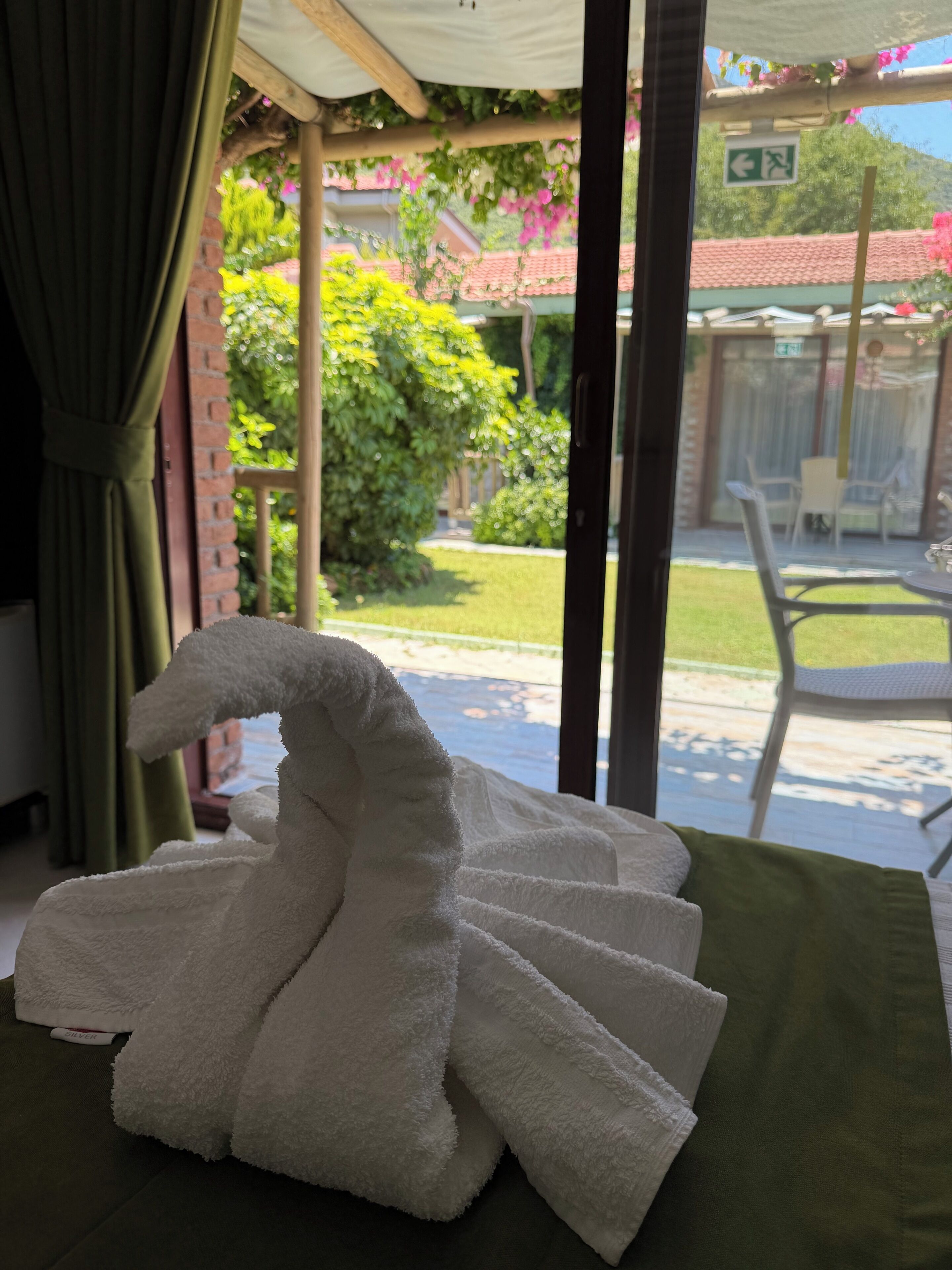 Een kamer met een bed, een raam met gordijnen en uitzicht op een tuin en een gebouw.