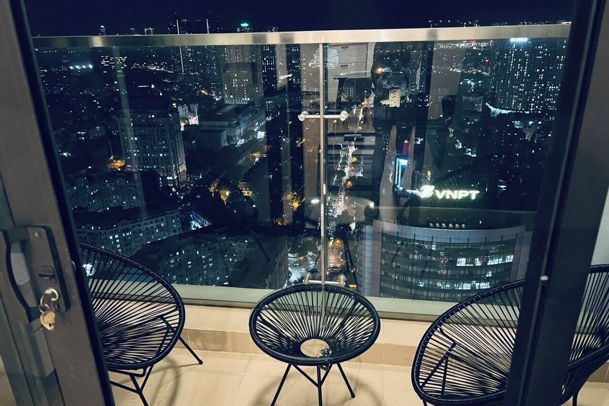 Een balkon met uitzicht op de stad 's nachts, met twee zwarte draadstoelen en een glazen deur.