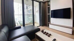 Ein modernes Wohnzimmer mit einer Couch, einem Couchtisch mit Teekannen, einer Fernbedienung, einem Deckenventilator und einem an der Wand montierten Fernseher.