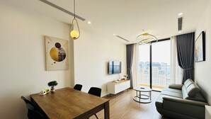 Ein modernes Wohnzimmer mit einem Holzesstisch, schwarzen Stühlen, einem grauen Sofa und einem Fernseher auf einer weißen Kommode.