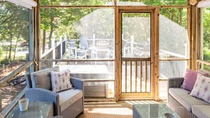 Ein überdachter Außenbereich mit Korbmöbeln und einem Glastisch, mit Blick auf eine Terrasse und Gartenmöbel.
