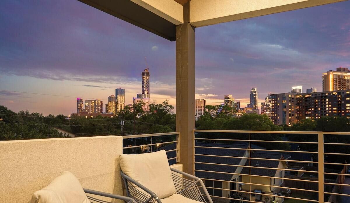 A balcony with a city skyline view, a chair, and a railing.