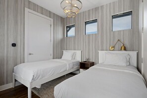 A bedroom with two single beds, a white door, a small bedside table with a lamp, and a window.
