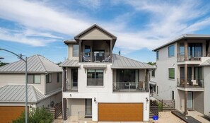 A modern two-story residential building with a garage, a balcony on the upper floor, and a second-story balcony with outdoor seating.