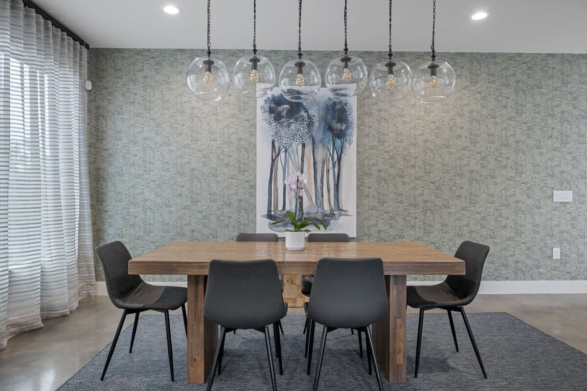 Un coin repas avec une table en bois, six chaises, une grande peinture abstraite et des lampes suspendues.