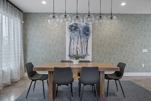 A dining area with a wooden table, six chairs, a large abstract painting, and hanging pendant lights.
