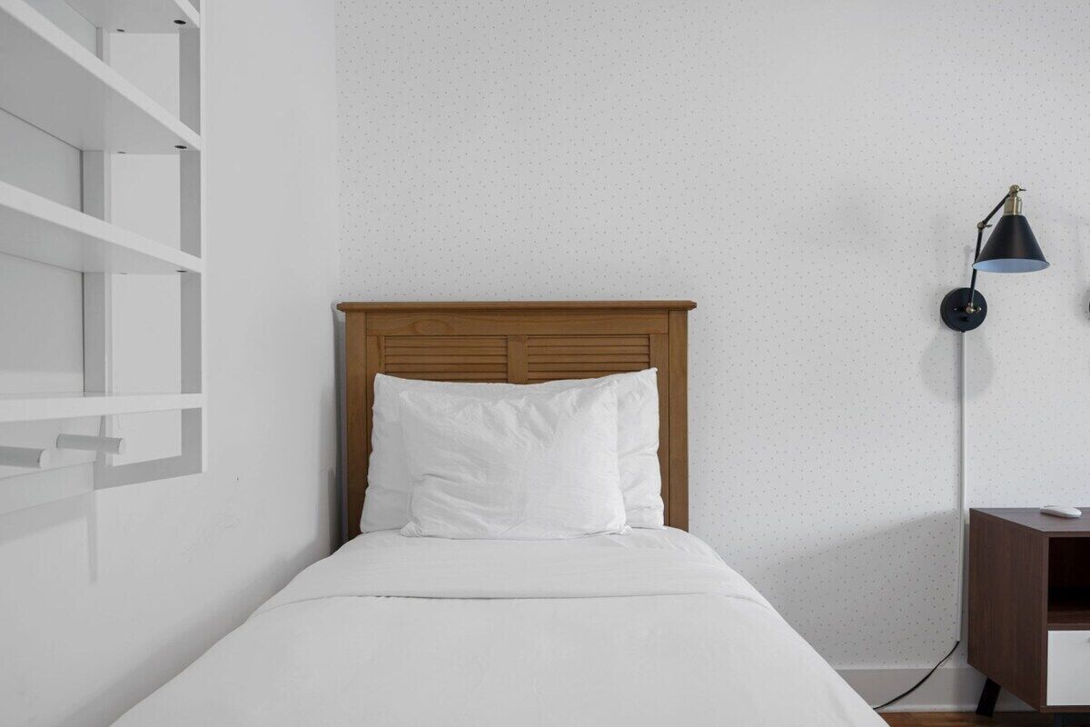A bed with a wooden headboard, white bedding, and a nightstand with a lamp.