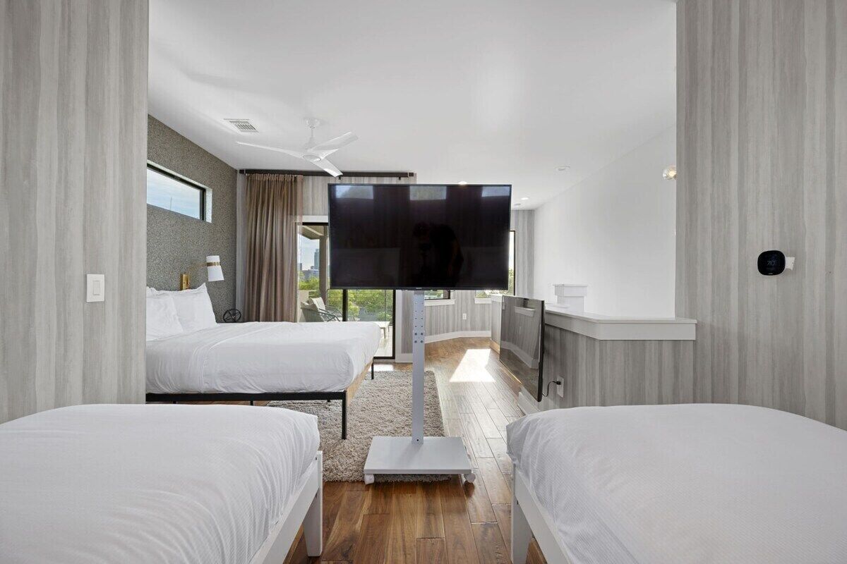 A hotel room with two beds, a flat-screen TV, a ceiling fan, and a view of the outdoors.