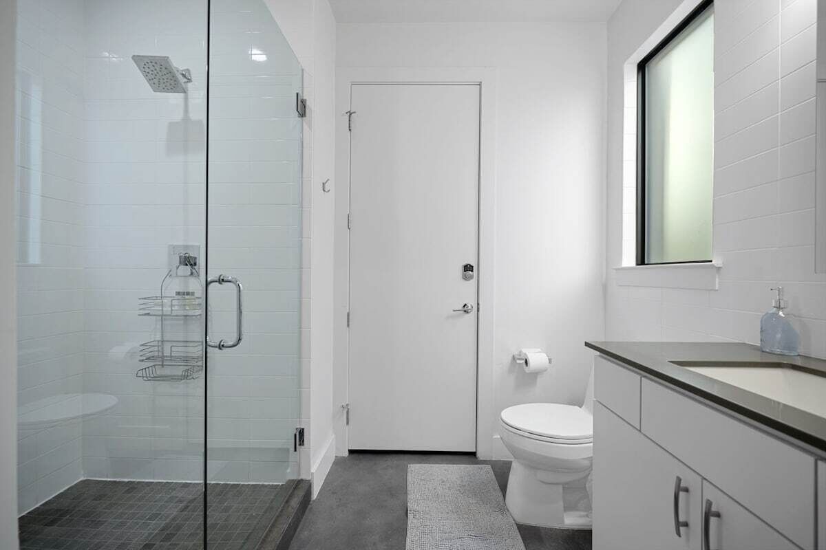 A modern bathroom with a glass shower enclosure, a toilet, and a sink with a mirror above.