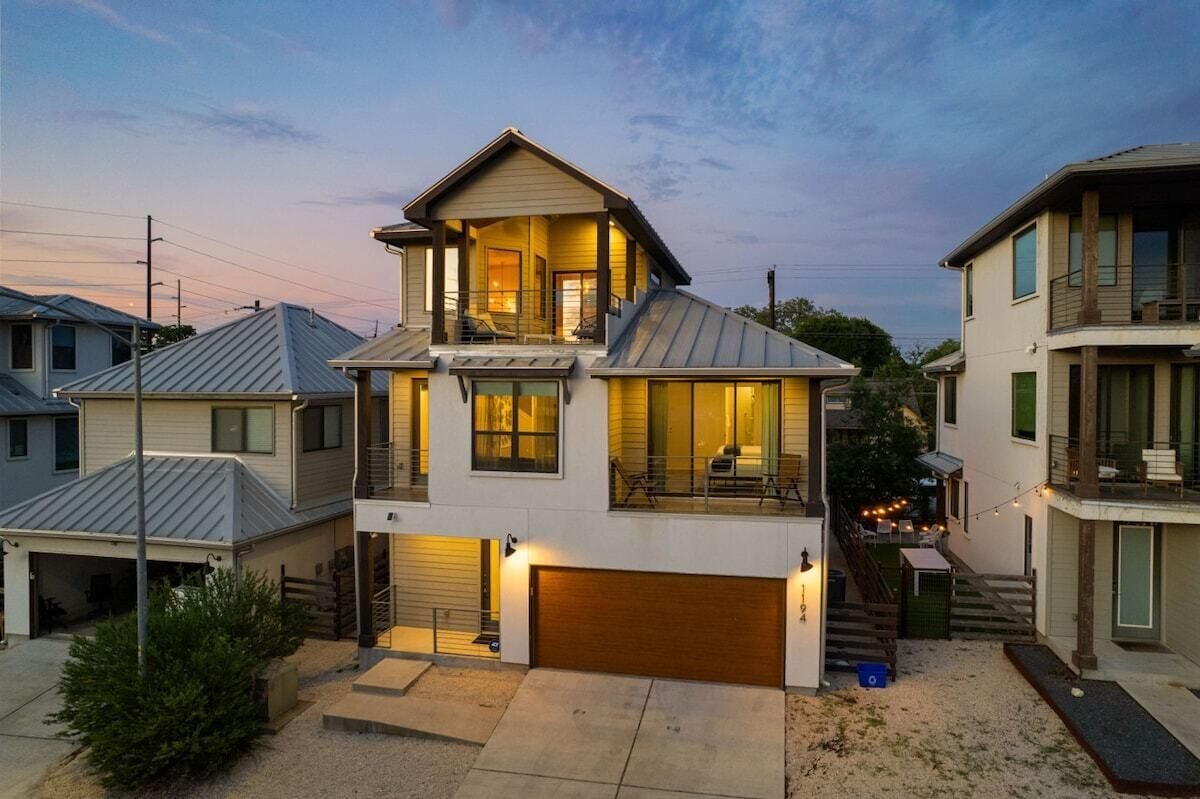 A two-story residential building with a garage, a balcony, and a covered outdoor seating area.