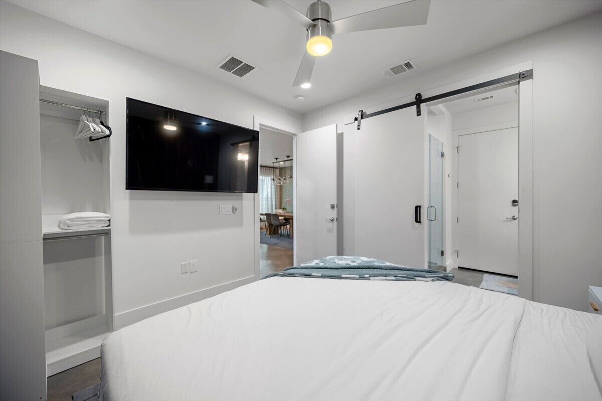 A modern bedroom with a bed, a wardrobe, a mirror, and a ceiling fan.