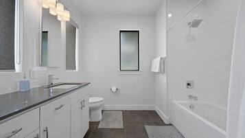 A modern bathroom with a large mirror, a toilet, a bathtub, and a shower.