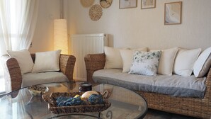 Ein Wohnzimmer mit Korbmöbeln, einem Glastisch und Wandbildern.