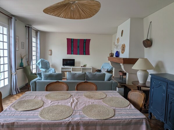 A living room with a sofa, TV, decorative wall, and a dining area with placemats.