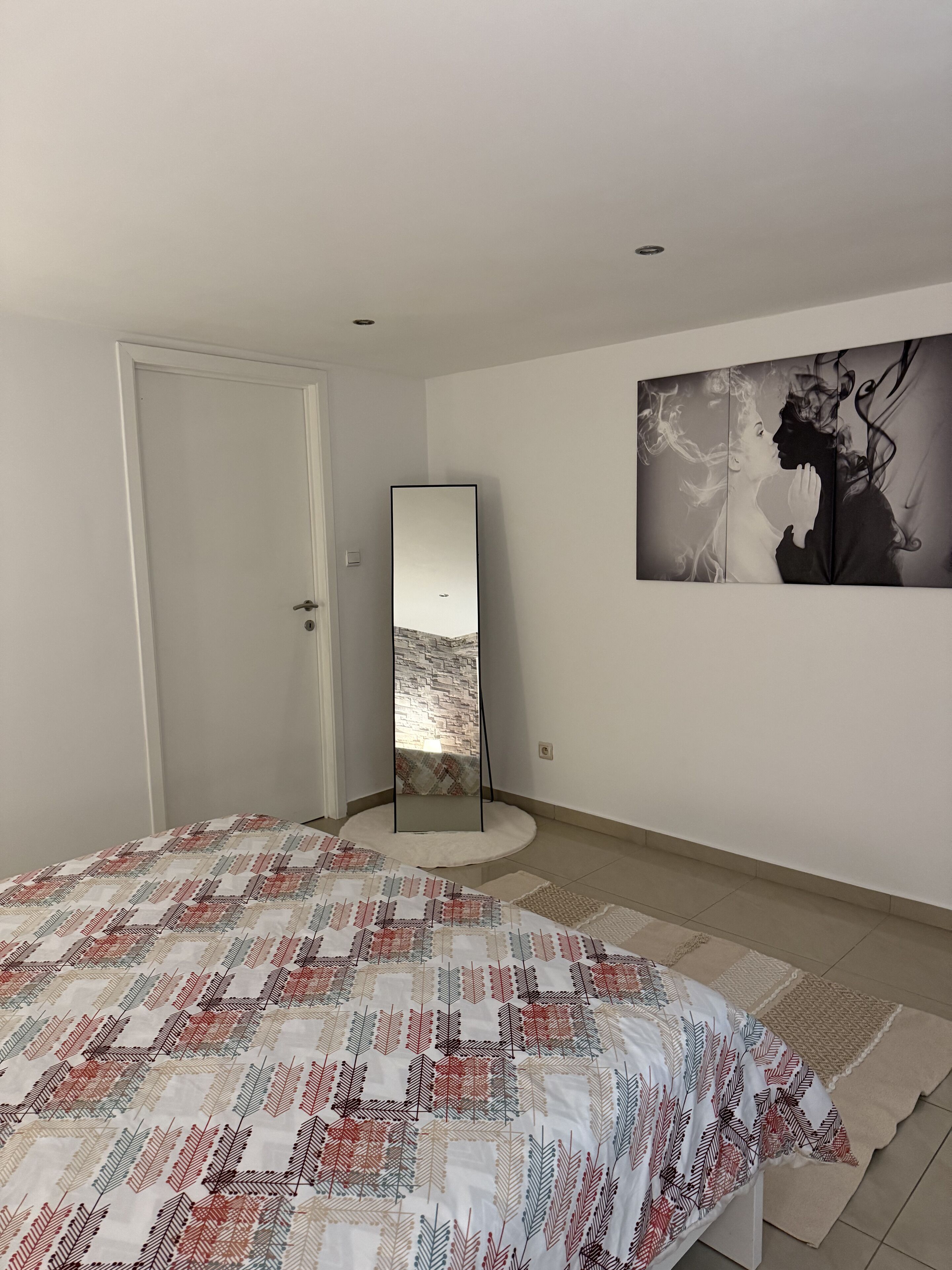Ein Schlafzimmer mit einem Bett, einem Stehspiegel und einem Wandbild.