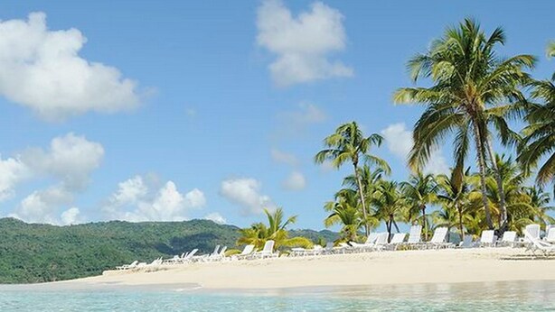 Ein Strand mit klarem türkisblauem Wasser, Palmen und einem Sandstrand.
