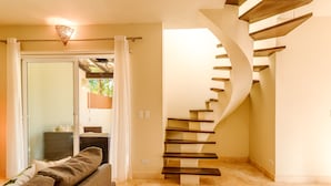 Ein modernes Interieur mit einer geschwungenen Holztreppe, einer Glastür, die zu einem Außenbereich führt, und einer gemütlichen Sitzecke mit Sofa und Kissen.