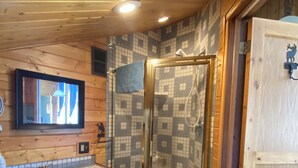 A wooden cabin bathroom with a glass shower, wooden cabinets, and a tiled backsplash. - Southfork Guesthouse (Cody)