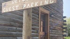 A wooden sign with the words "Welcome Guest Parking" in front of a log cabin with a wooden door and a lantern on the wall. - Southfork Guesthouse (Cody)