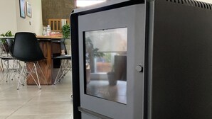 A modern kitchen with a built-in wood stove, a dining area with chairs and a table, and a visible window.