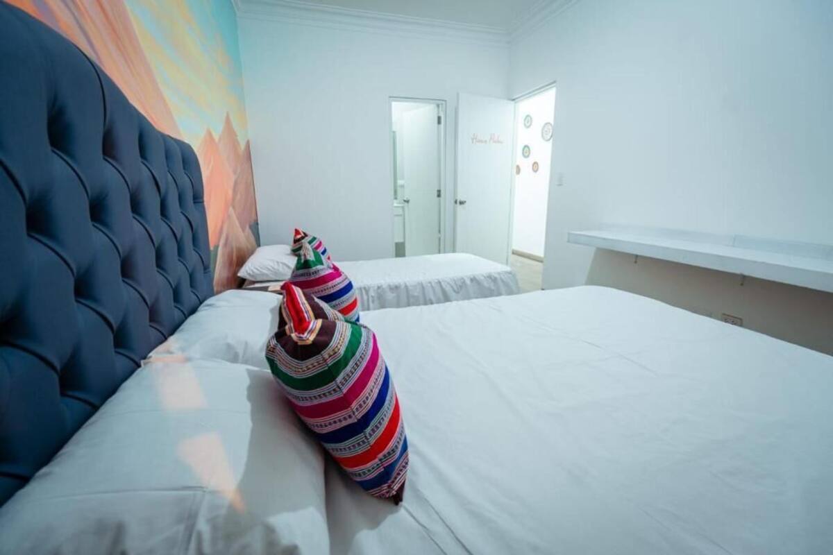Una camera d'albergo con una grande testiera imbottita, due letti singoli e una coperta a righe colorate.