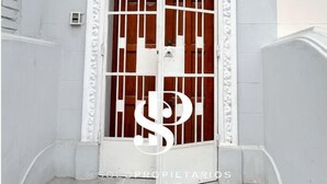 A white metal gate with a decorative pattern, a wooden door, and a number '190' on the wall. - Casa Águila y Condor (Lima)