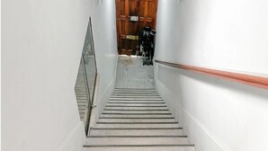 A staircase with a handrail, leading to a room with a wooden door and a black object on the floor. - Casa Águila y Condor (Lima)