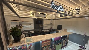 A reception area with a sign, a reception desk, a potted plant, and a wall with colorful artwork. - Hostel A07 (Alanya)