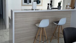 A modern kitchen with a central island, two bar stools, and a dining area with a table and chairs. - Elegant functional villa with saltwater pool (Torrevieja)