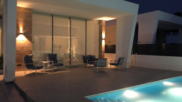 A modern outdoor pool area with glass walls, seating, and ambient lighting. - Elegant functional villa with saltwater pool (Torrevieja)
