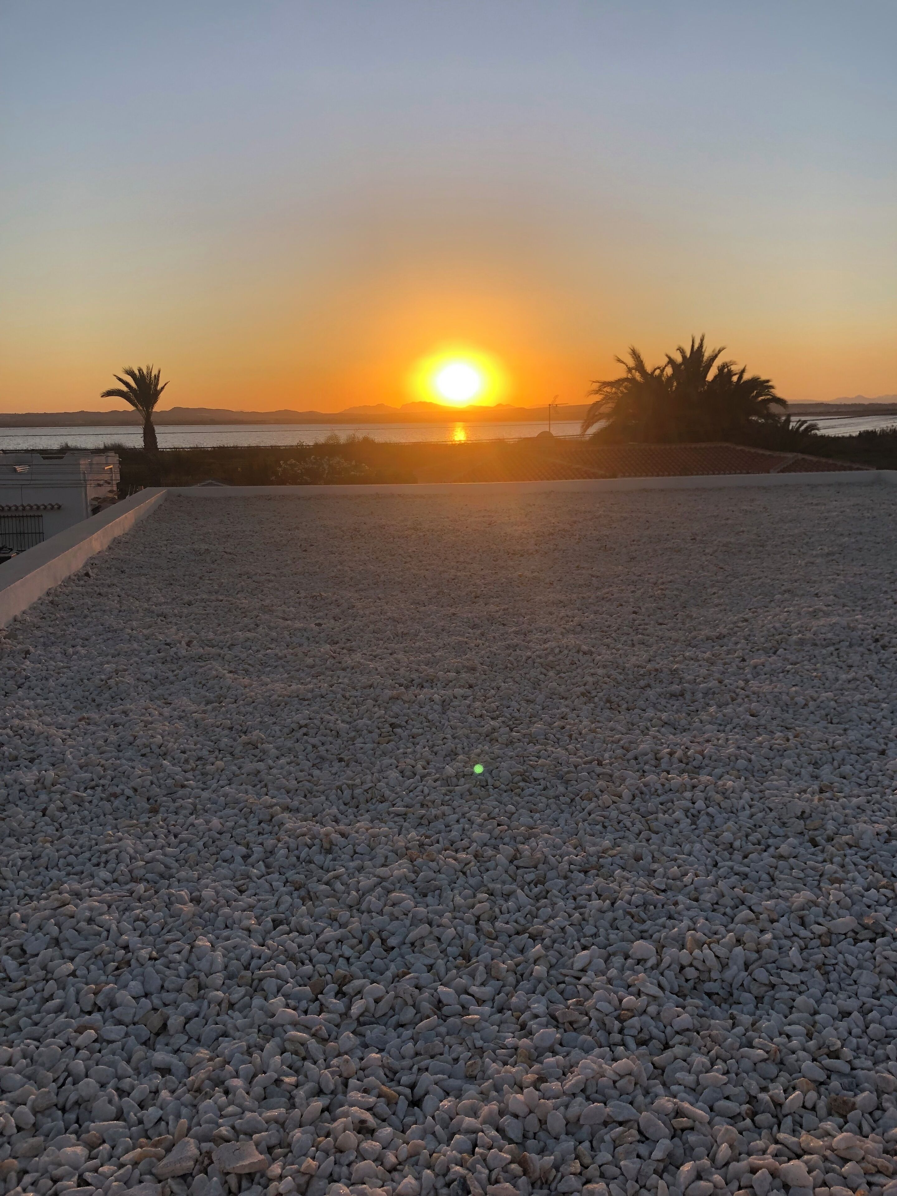 A pebbled terrace with a sunset view over a body of water and distant mountains.