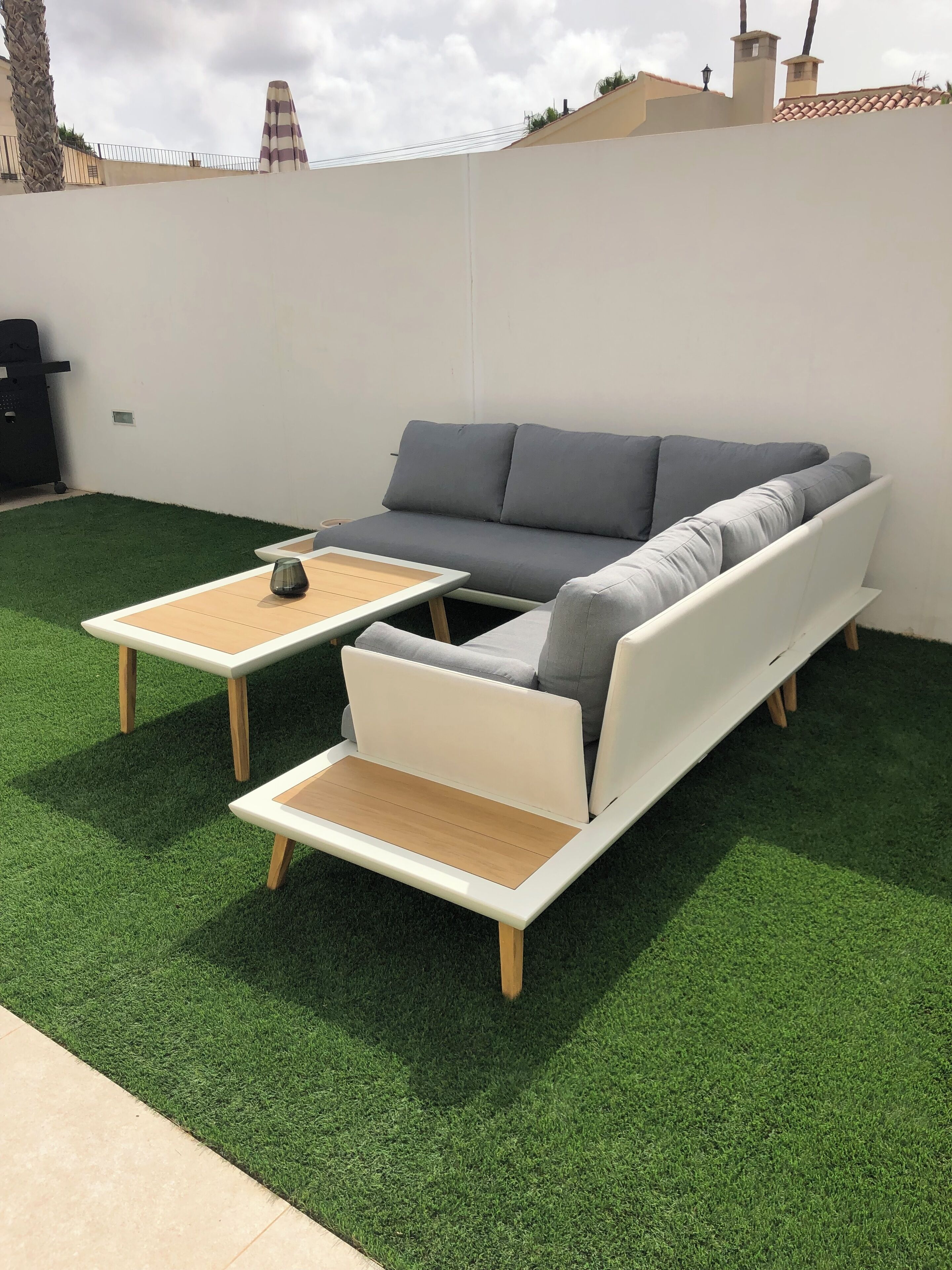 A modern outdoor seating area with a sofa and two tables on artificial grass.