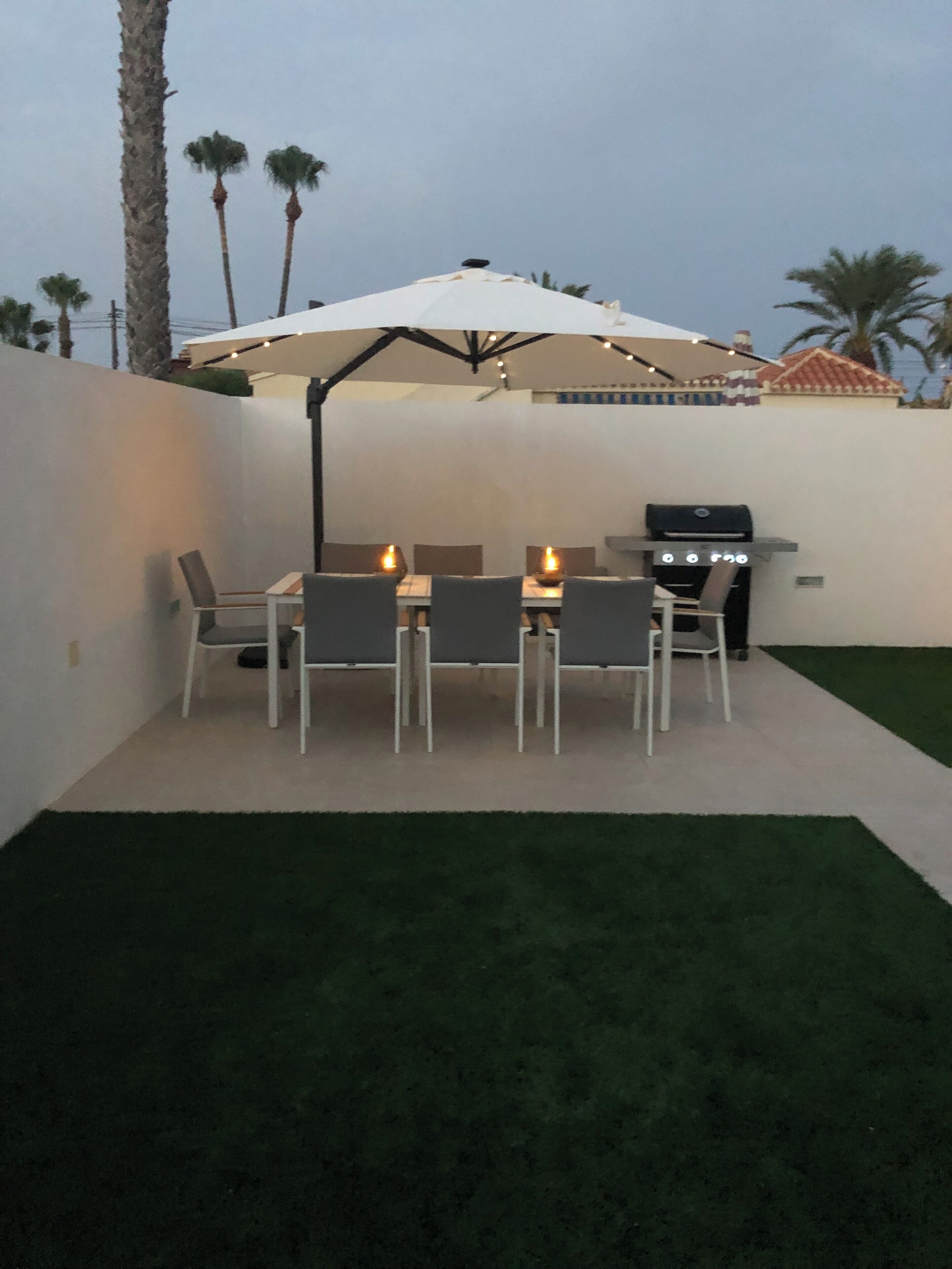 Une terrasse extérieure avec une table et des chaises, un barbecue et des guirlandes lumineuses.