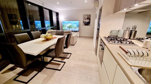 Una cocina moderna con estufa a gas, un comedor con mesa y sillas, y vista a un puente a través de grandes ventanales.