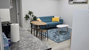 A compact living space with a kitchenette, a dining area with a table and chairs, a sofa with cushions, a small rug, and a refrigerator. - Cozy Family-sized basement suite. (Winnipeg)