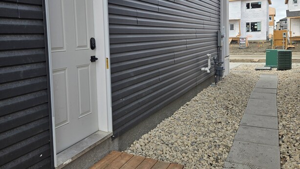 A residential building with a white door, a wooden bench, and a gravel pathway. - Cozy Family-sized basement suite. (Winnipeg)
